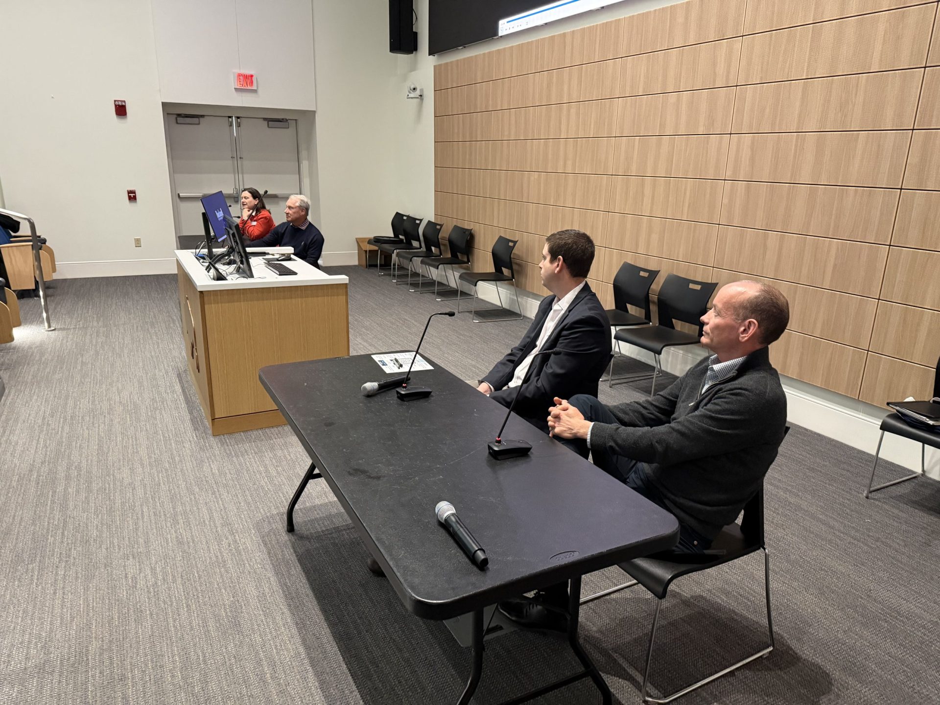Panel speakers sitting at two tables at the front of a lecture hall.